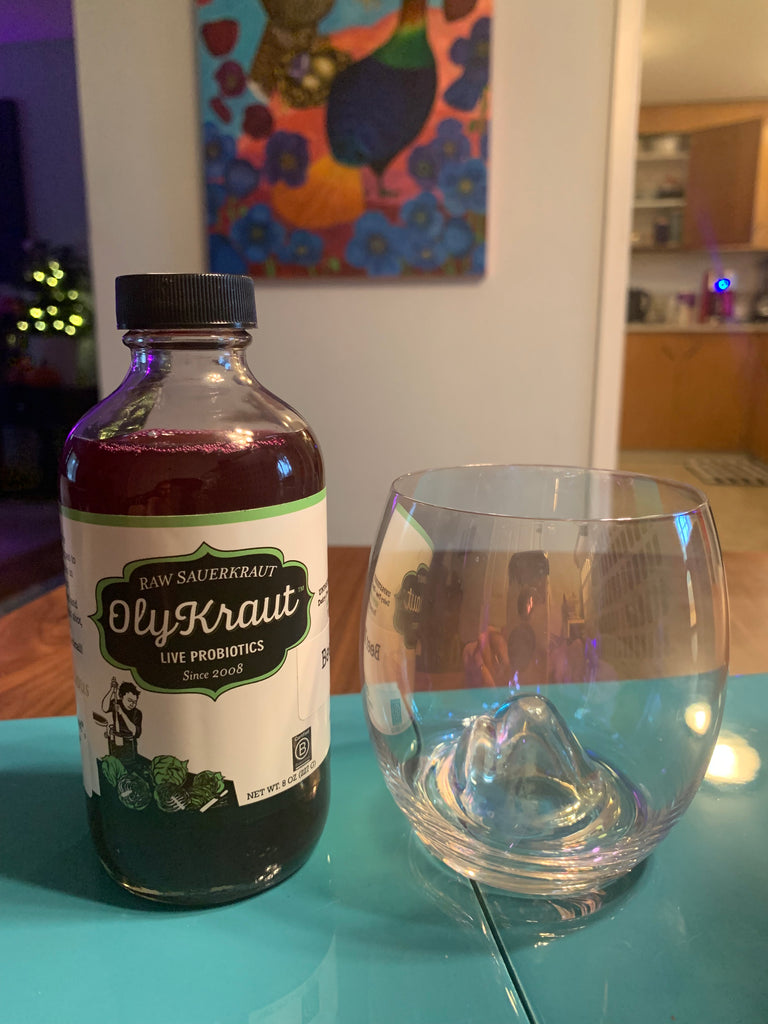 A bottle of OlyKraut Beet Kvass next to a clear glass, on a dining room table